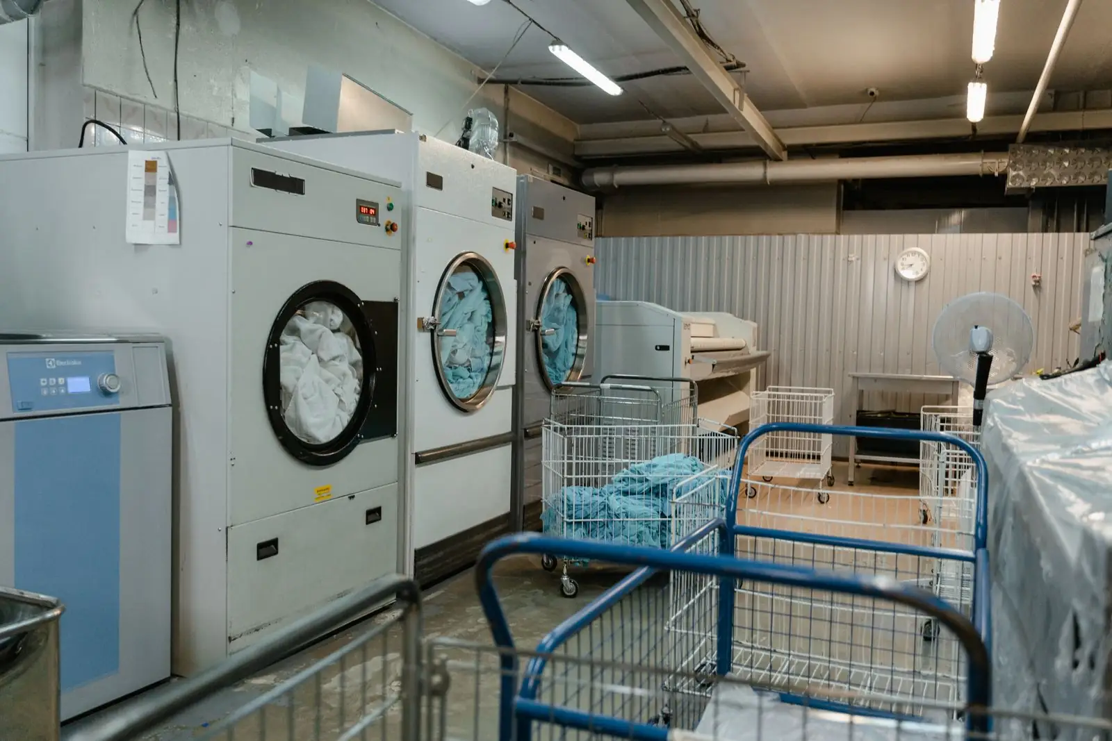 Commercial washing machines and laundry trolleys inside a laundry facility