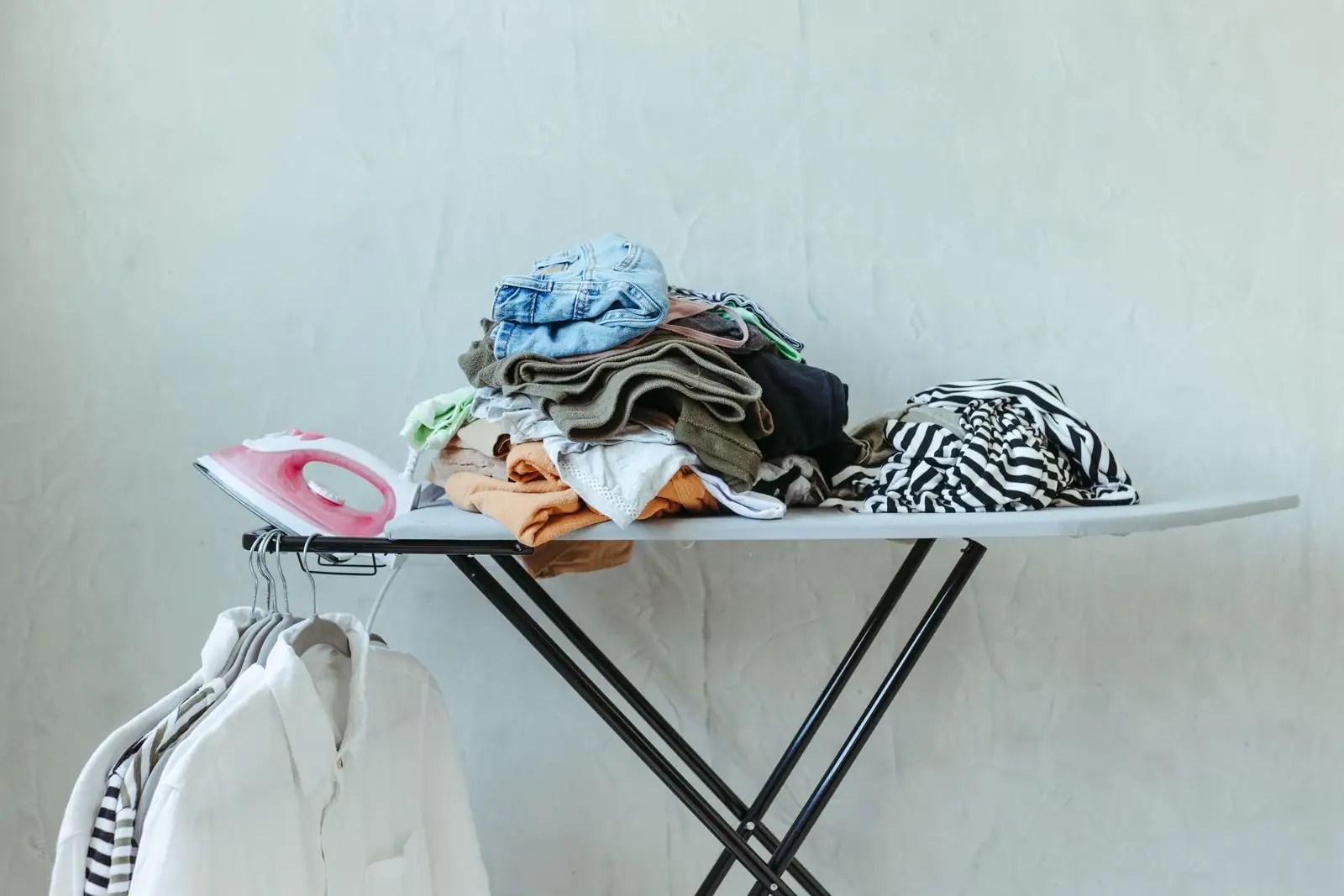Ironing board with sorted garments, an iron and pressed white shirts nearby