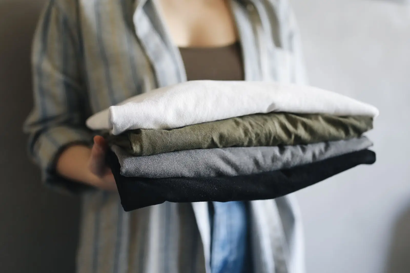 Hands holding a stack of neatly folded, freshly laundered clothes