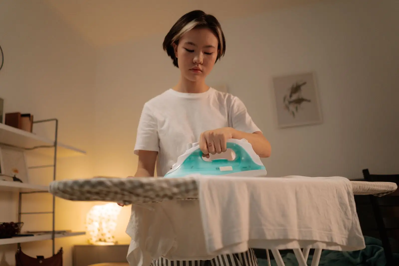 Person pressing a white shirt on an ironing board at home